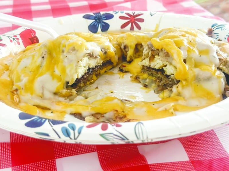 A biscuit with sausage covered in gravy and cheese on a paper plate.